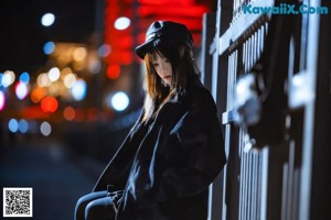 A woman in a black dress and hat standing in front of a fence.