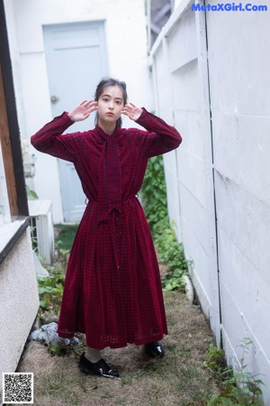 A woman in a red and black dress leaning against a wall.