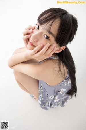 A woman sitting on the floor wearing a gray and white floral romper.