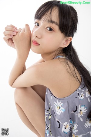 A woman standing in front of a white background wearing a gray floral romper.