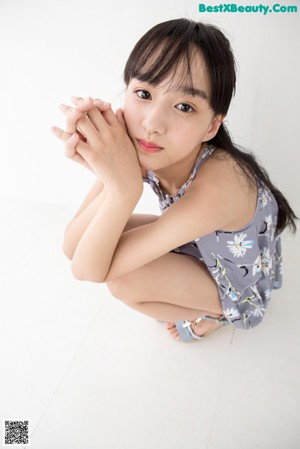 A woman sitting on the floor wearing a gray and white floral romper.