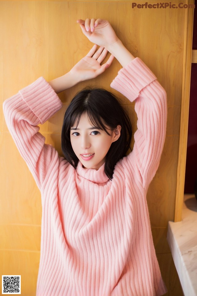 A woman in a pink sweater leaning against a wooden wall.