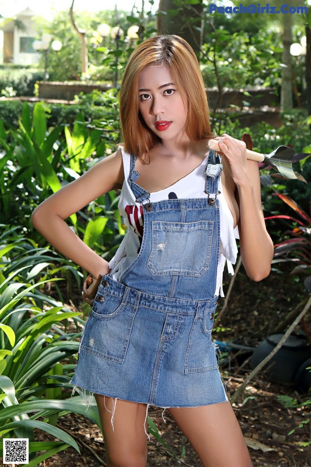 A woman in a denim dress holding a shovel.