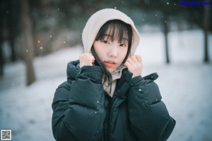 A woman in a black coat crouching down in the snow.