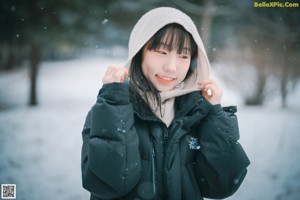 A woman in a black jacket and orange bikini sitting in the snow.