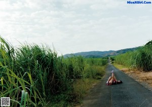 A woman sitting on the side of a road looking at her cell phone.