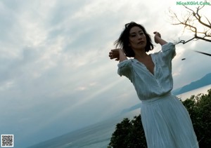 A woman standing in a grassy field with mountains in the background.