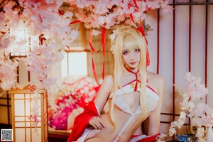 A woman in a red and white kimono sitting under a cherry blossom tree.