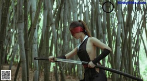 A woman holding a sword in a bamboo forest.