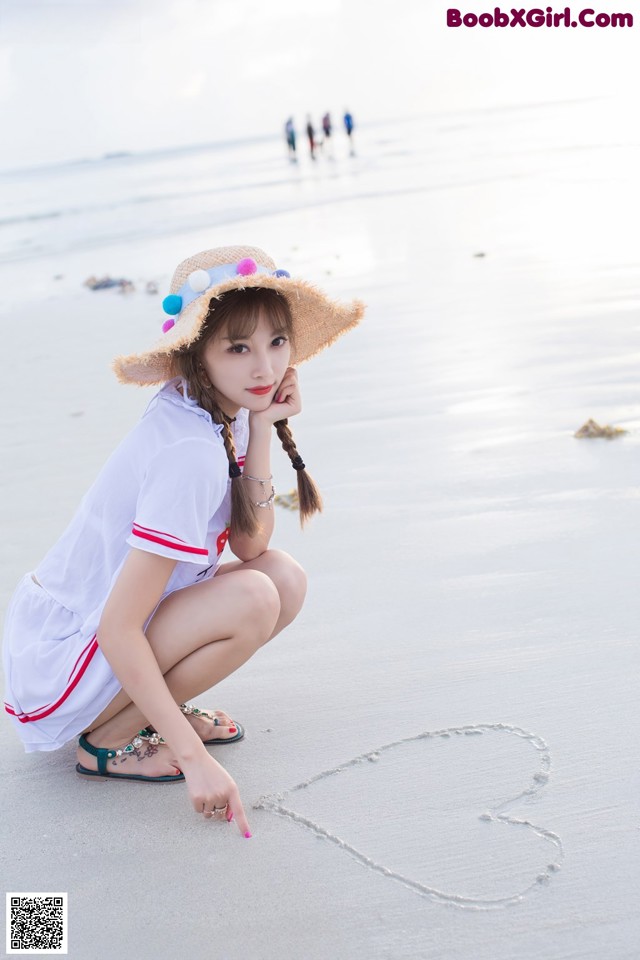 A woman kneeling on the beach with a heart drawn in the sand.