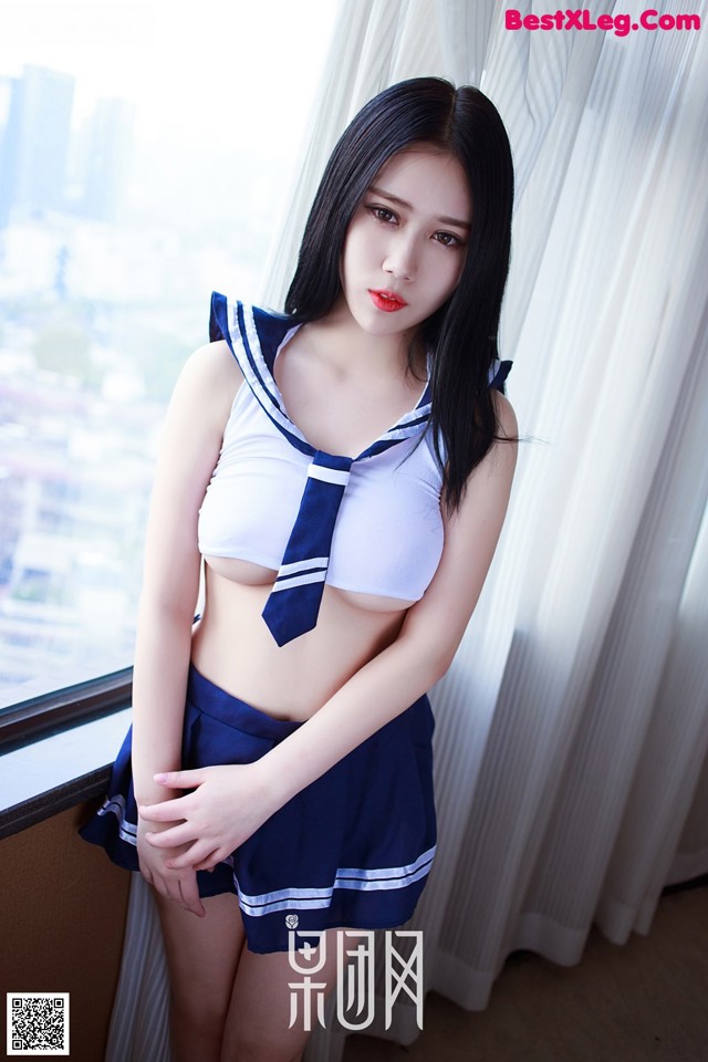 A woman in a sailor outfit posing by a window.
