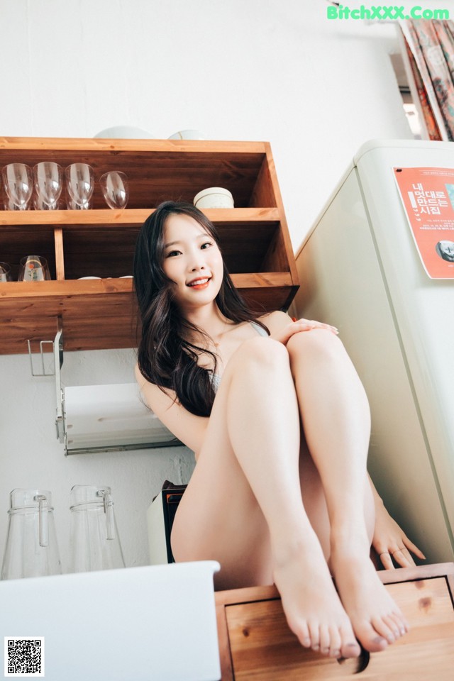 A woman sitting on top of a kitchen counter next to a refrigerator.