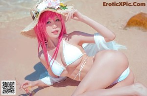 A woman in a bikini and a straw hat sitting in the water.