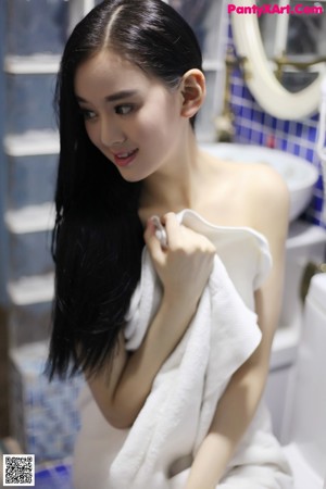 A woman in a white towel standing in a bathroom.