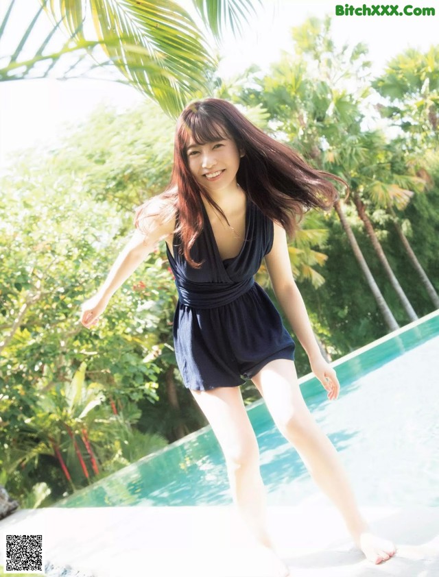 A woman in a black dress standing next to a swimming pool.