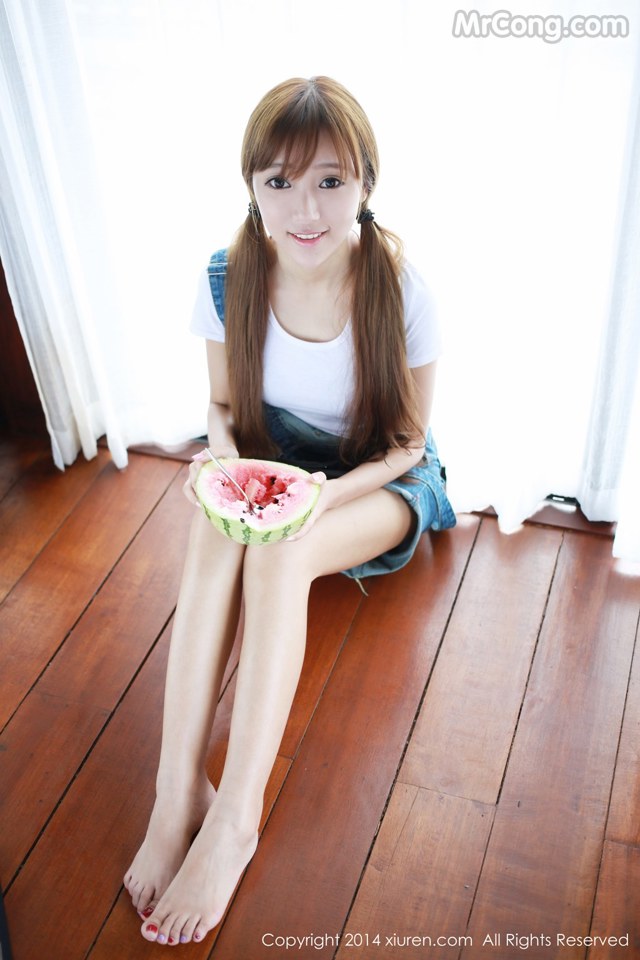 A woman sitting on the floor eating a slice of watermelon.