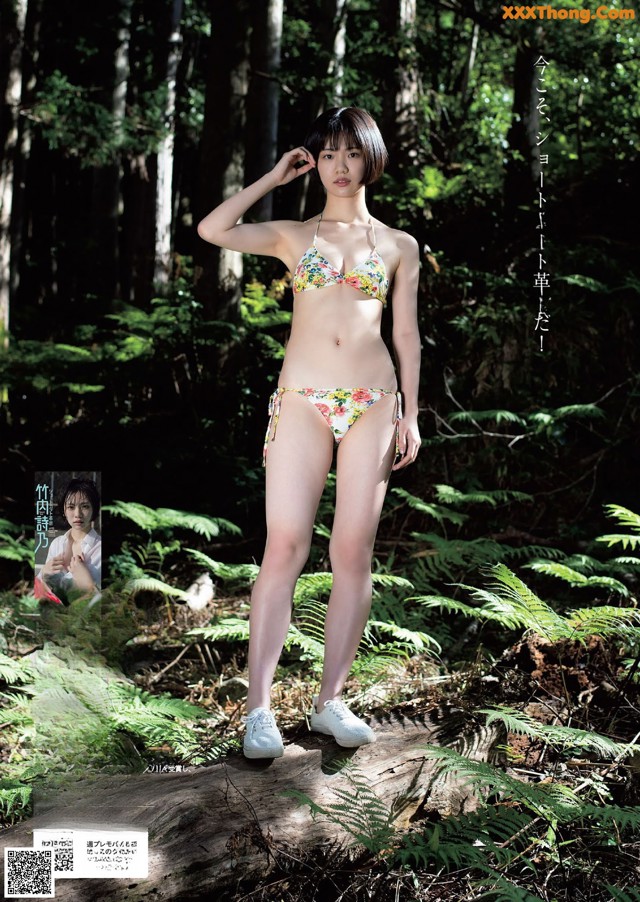 A woman in a bikini standing on a log in the woods.