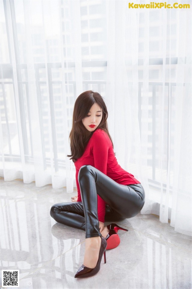 A woman in a red shirt and black pants sitting on the floor.