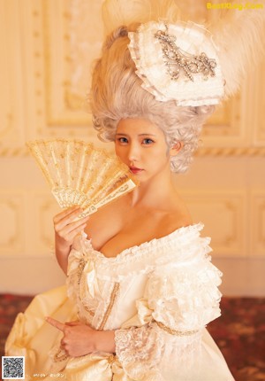 A woman in a white dress and hat sitting on a bed.