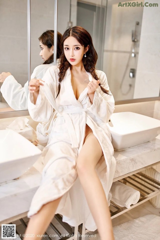 A woman in a white robe sitting on a bathroom counter.