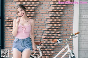 A woman in a pink top and denim shorts holding an umbrella.