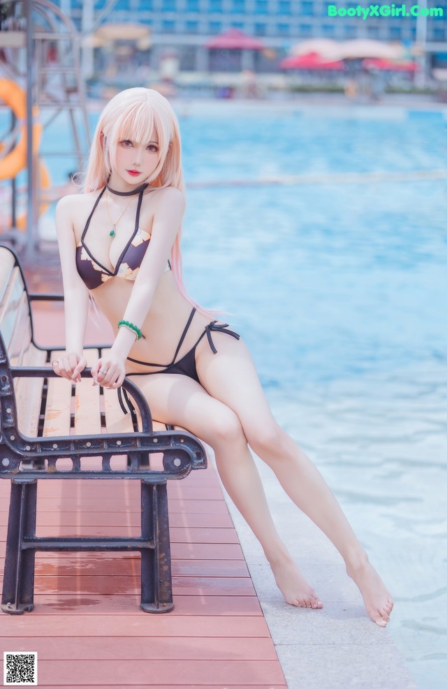 A woman in a bikini sitting on a bench by the water.