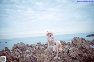 A woman with pink hair sitting on a rock by the ocean.