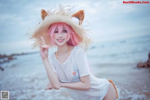 A woman with pink hair sitting on a rock by the ocean.