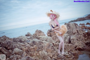 A woman with pink hair sitting on a rock by the ocean.