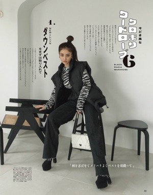 A woman sitting on a stool wearing a brown jacket and jeans.