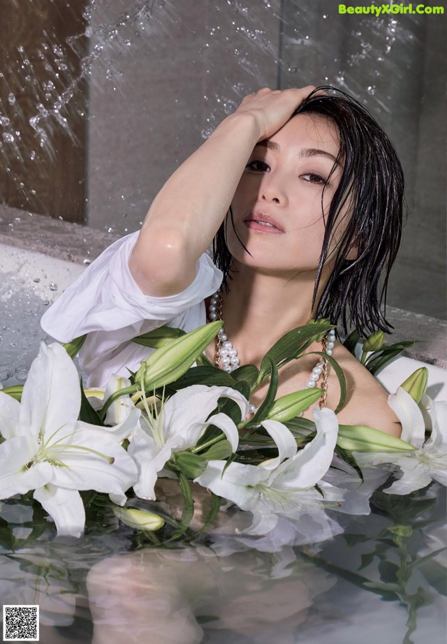 A woman in a bathtub with white flowers in the water.