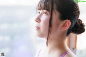 A woman in a pink swimsuit standing by a window.