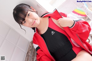 a woman in a red jacket and black leotard leaning against a wall
