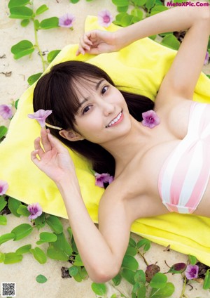 A woman in a pink bikini laying on a log on the beach.