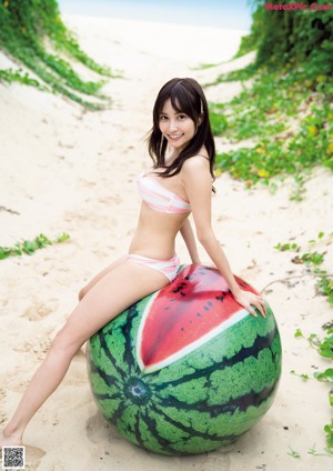 A woman in a pink bikini laying on a log on the beach.