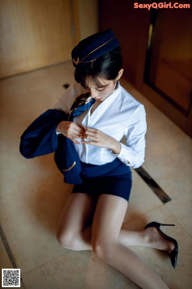 A woman in a blue uniform is sitting on the floor.
