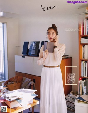 A woman sitting on a couch wearing a white dress and sneakers.